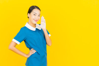 Portrait of smiling young woman standing against yellow background