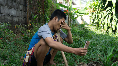 Young man using mobile phone while sitting on plants