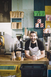 Portrait of smiling male retail clerk leaning on checkout counter at grocery store