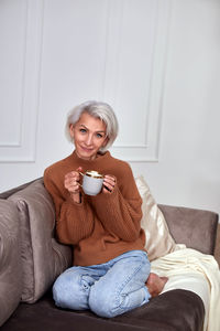 Cheerful female sitting with cup of tea on comfortable sofa