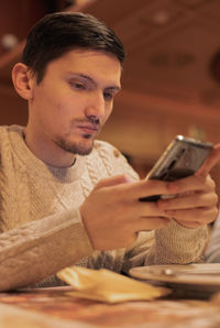 Portrait of a young guy with a phone sitting at the table.