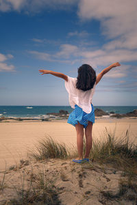 Rear view of woman standing at beach with arms open to the wind