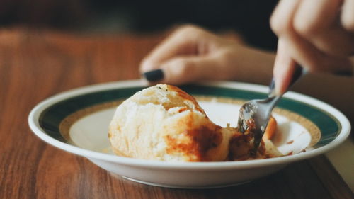 Cropped hand holding fork in food plate on table