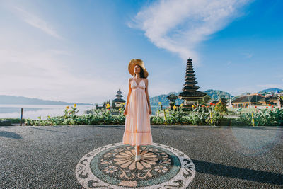 Woman standing at pura ulu danau temple against sky during sunrise