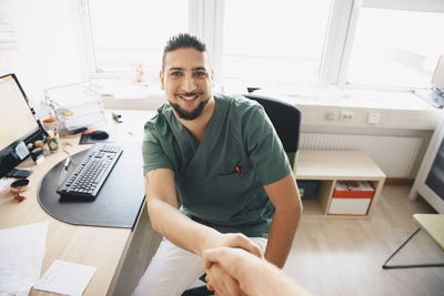 Portrait of smiling young male nurse shaking hands with doctor at office in hospital