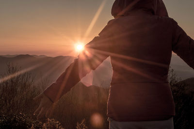 Rear view of man standing on field against sky during sunset