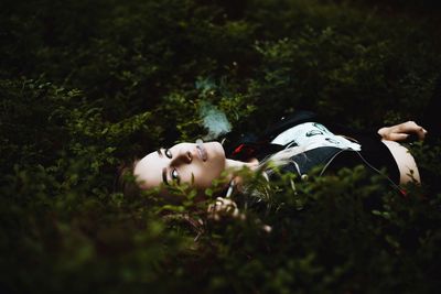 Portrait of young woman smoking while lying on plants