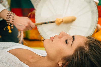 Cropped hand of therapist playing drum by young woman at spa