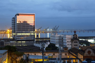 Illuminated factory by sea against sky in city