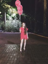 Full length of woman with pink balloons standing against trees