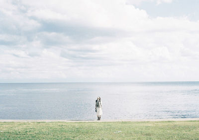 Woman standing on sea shore against sky
