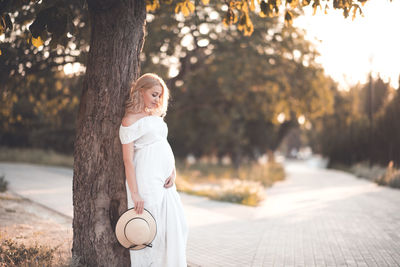 Pregnant woman leaning on tree at park during sunset