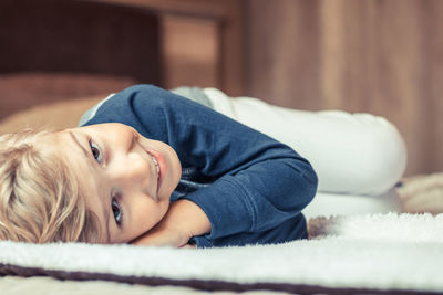 High angle portrait of cute smiling boy lying on bed at home