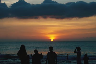 Silhouette people on beach against sky during sunset