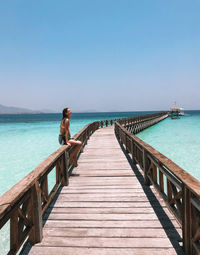 Woman sitting on pier over sea against clear sky