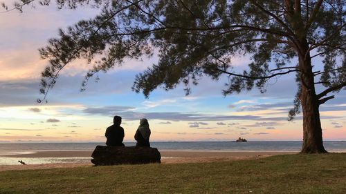 Silhouette people sitting on beach against sky during sunset