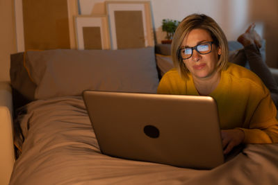 Young woman using laptop while sitting on bed at home