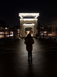 Rear view of woman standing on illuminated street at night