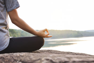 Cropped image of woman practicing yoga while sitting on rock