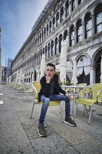 Full length of young man sitting on seat in city
