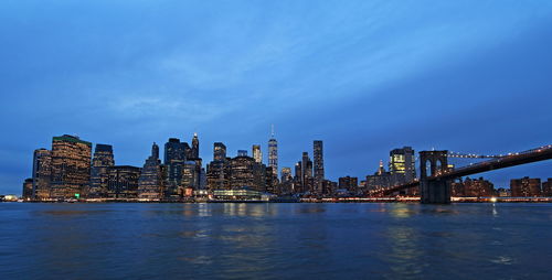 Illuminated city at waterfront against blue sky