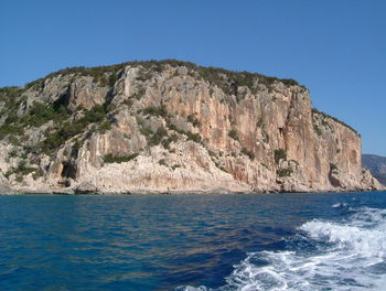 Rock formations in sea against clear blue sky