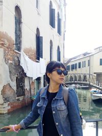 Young woman wearing sunglasses standing against buildings in city