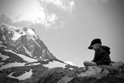 Rear view of woman sitting on rock against sky