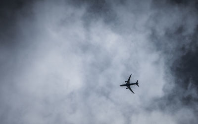 Low angle view of airplane flying against cloudy sky