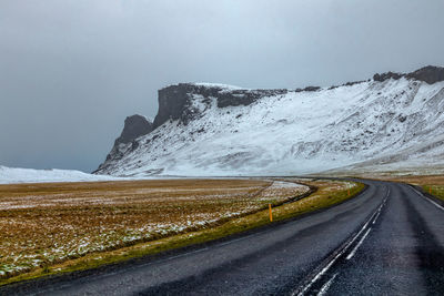 Road leading towards snowcapped mountain against sky