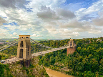 A view of a suspension bridge with a dramatic cloudy sky.