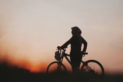 Silhouette person riding bicycle against sky during sunset