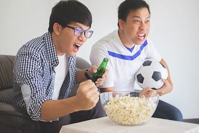 Father and son watching tv with snacks and soccer ball at home