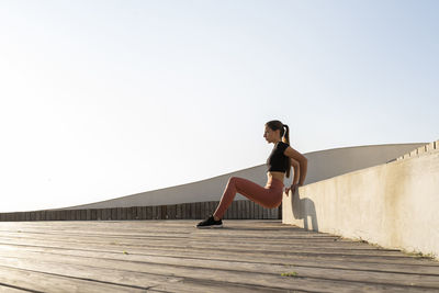 Female athlete doing bench press position on promenade against clear sky