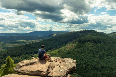 Rear view of man sitting on rock against sky