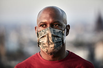 Bald man wearing protective face mask while looking away at rooftop against sky during coronavirus