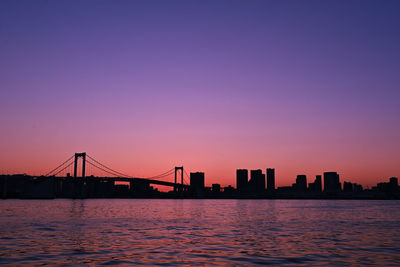 Silhouette bridge over river against sky during sunset