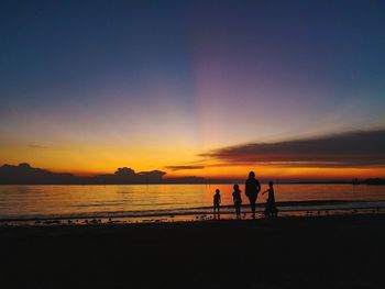 Silhouette people on beach against sky during sunset