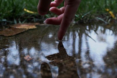 Cropped finger of woman touching water in puddle