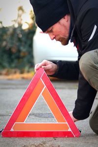 Midsection of man positioning red safety triangle  while standing on street