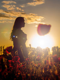 Girl stands in poppy field at sunset