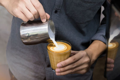 Midsection of man pouring cream in coffee