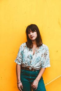 Portrait of beautiful young woman standing against yellow wall