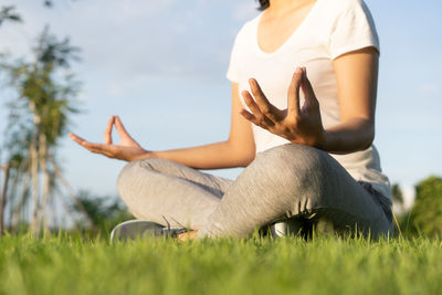 Low section of woman sitting on field against sky