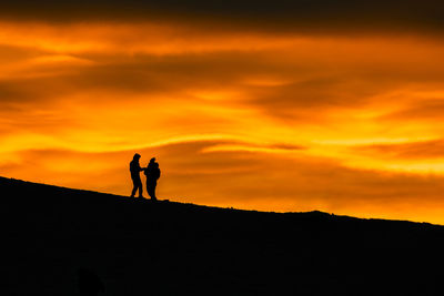 Silhouette people standing against orange sky during sunset