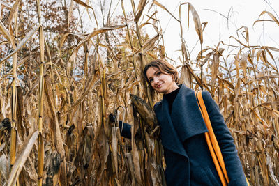 Woman hugging dry corn stalks in cornfield in autumn