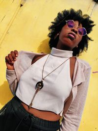 Portrait of young woman wearing sunglasses while standing against wall