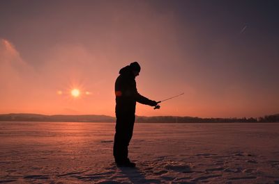 Silhouette man fishing at sunset