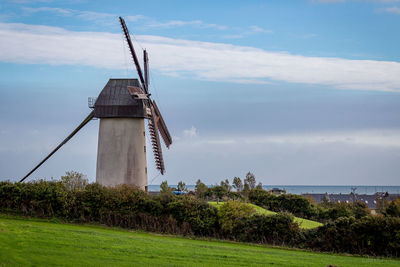 Traditional windmill on grassy field by river against sky