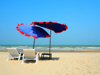 Lounge chairs on beach against clear blue sky